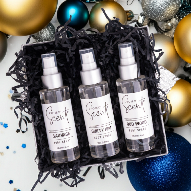 Three spray bottles labeled 'Project Scent' surrounded by colorful Christmas ornaments on a white background.