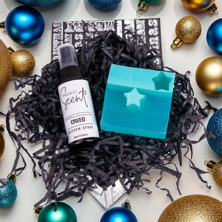 Decorative arrangement of Christmas ornaments with a Creed product in the center.