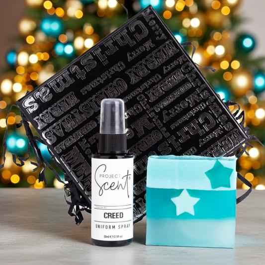 Bottle of 'Project Scent' Creed Uniform Spray with a black textured box and blue star-patterned Soap Bar against a blurred festive background.