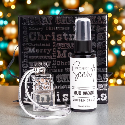 Project Scent Oud Wood uniform spray bottle with a Christmas-themed gift box and car air freshener in front of a decorated Christmas tree.