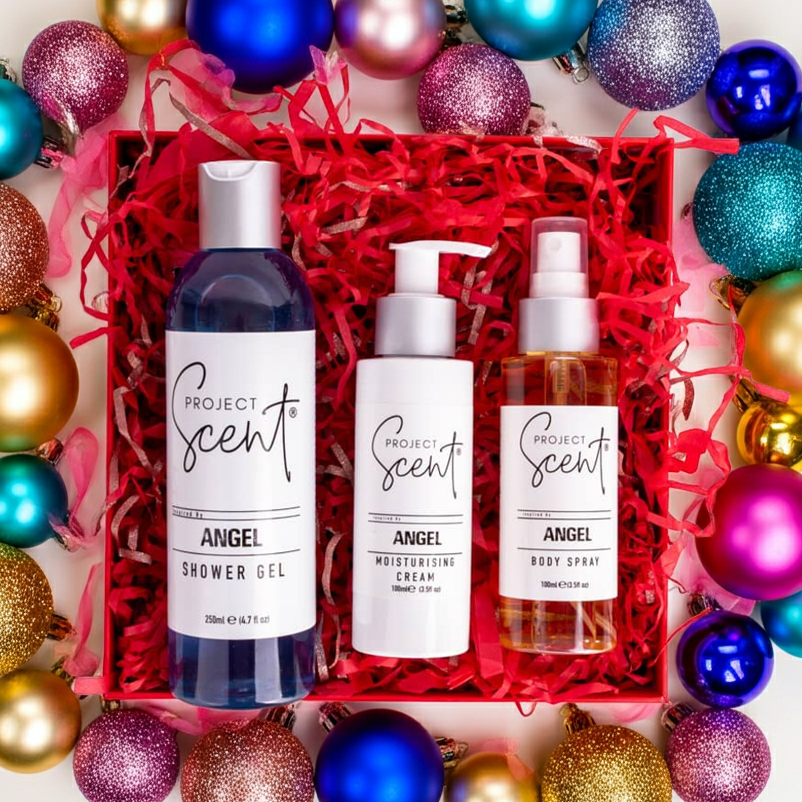 Flatlay of Christmas body care gift set surrounded by festive decorations. Features handmade shower gel, moisturising cream and body spray gift box.