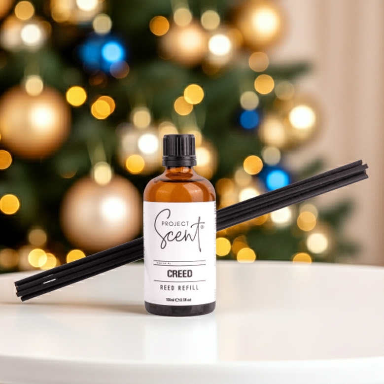 Bottle of Creed Project Scent Reed Diffuser Refill with black reeds on a marble surface with a Christmas tree in the background