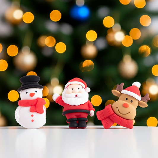 Three Christmas-themed figurines (snowman, Santa Claus, reindeer) in front of a blurred Christmas tree with lights.