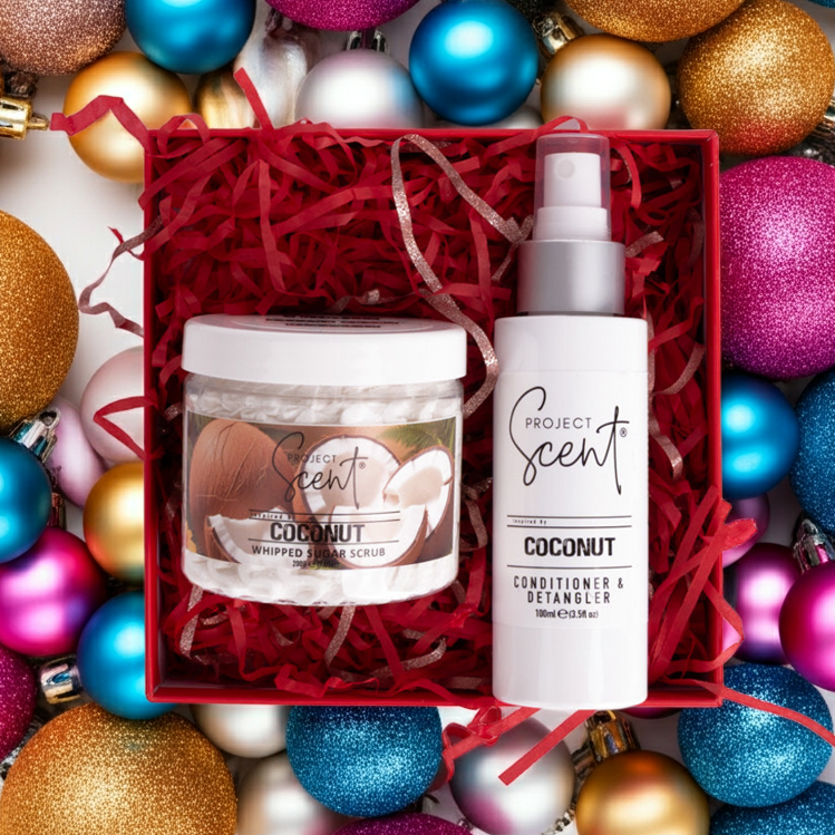 Flatlay of Christmas body and hair gift set surrounded by festive decorations. Features handmade whipped sugar scrub and leave-in conditioner gift box.