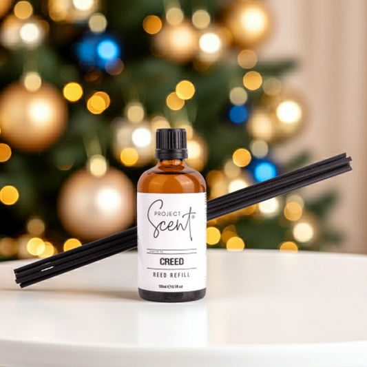 Bottle of Creed Project Scent Reed Diffuser Refill with black reeds on a marble surface with a Christmas tree in the background